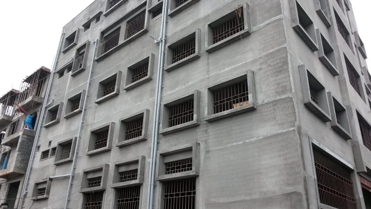 Multi-storey building exterior with window grilles and unfinished plasterwork