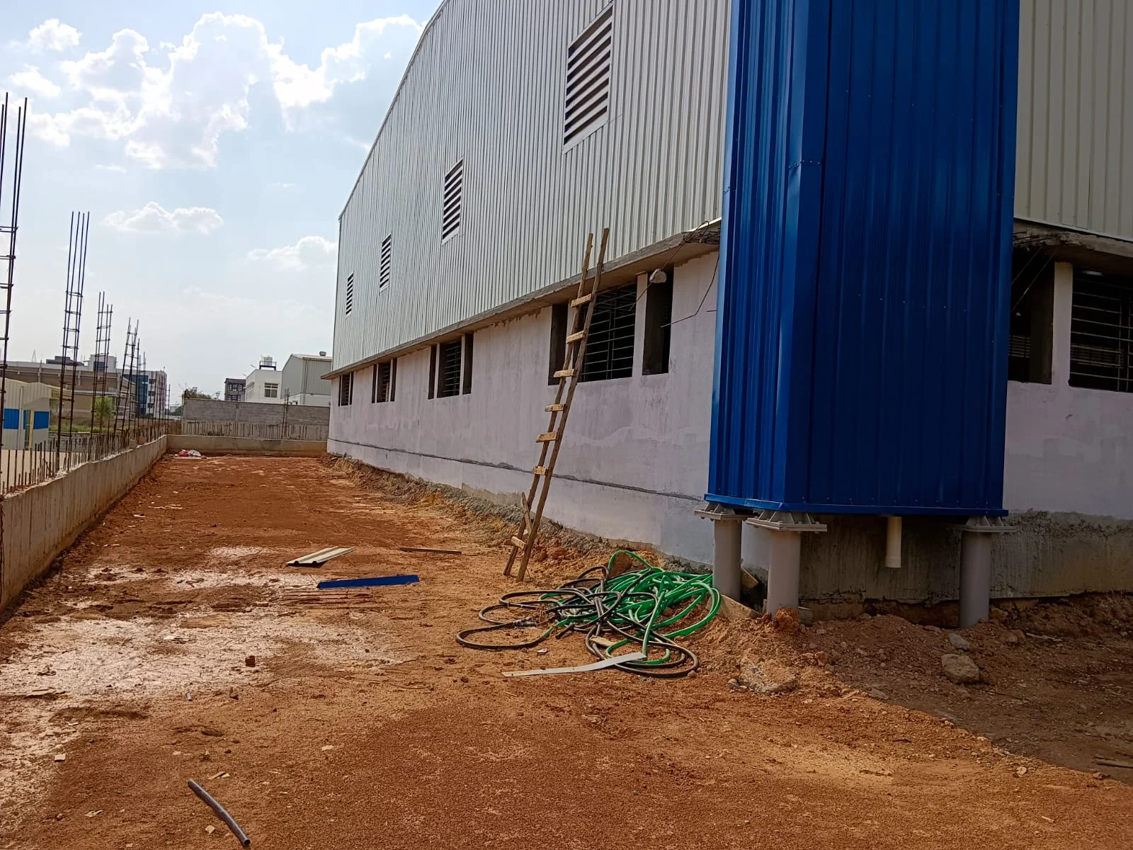 Factory side with blue rainwater piping and compound wall under construction